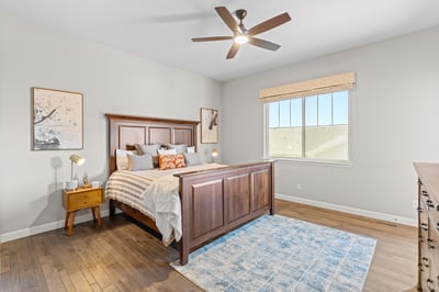Bright and inviting bedroom featuring a wooden bed frame, large window, and cozy decor elements.