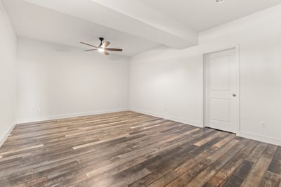Spacious room featuring warm wood flooring, a ceiling fan, and natural light options for customization.