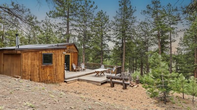 Cozy cabin nestled among towering pines, featuring an inviting deck for outdoor relaxation and enjoyment.