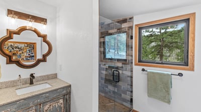 Bright bathroom featuring a modern glass shower and a beautifully framed mirror, with nature views beyond.