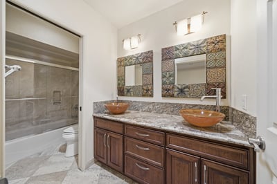 Bright bathroom featuring dual vessel sinks, modern fixtures, and a spacious layout with stylish tile accents.