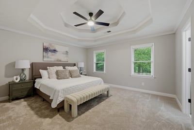 Spacious primary bedroom featuring a tray ceiling, natural light, and comfortable seating for relaxation.
