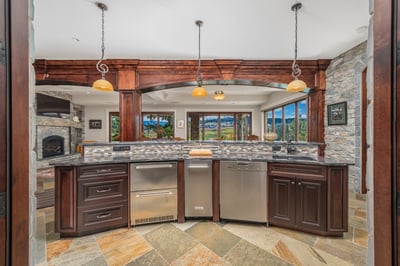 The full bar/wine cellar incorporates a modern kitchen with stone accents, expansive views, and high-end appliances, perfect for entertaining and gatherings.