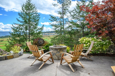Cozy outdoor patio featuring a stone fire pit, next to the pool fountain, surrounded by greenery, and with stunning panoramic views.
