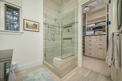 Modern bathroom featuring a spacious glass shower, neutral tones, and ample storage in a nearby large closet with extensive cabinetry.