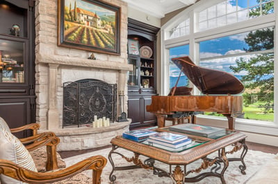 This inviting living space features a grand piano, stone fireplace, and picturesque window views of the outdoors.