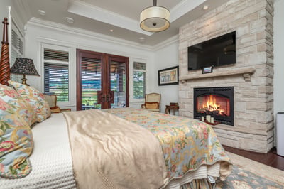 Primary bedroom featuring a fireplace, comfortable seating, and access to an outdoor balcony with views through French doors.