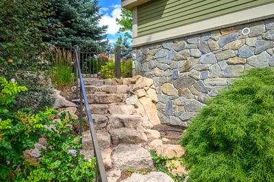 Discover a beautifully landscaped entryway featuring natural stone steps and lush greenery, inviting you home.