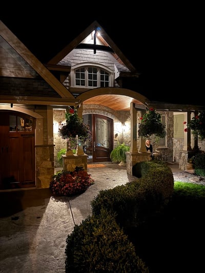 This welcoming home features a beautifully lit entrance, showcasing exquisite stonework and vibrant landscaping.