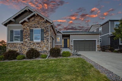 Modern stone-front home featuring a spacious driveway, well-maintained landscaping, and vibrant sunset views.