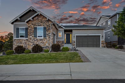 Modern home featuring stone accents, solar panels, and a spacious driveway with picturesque sunset views.