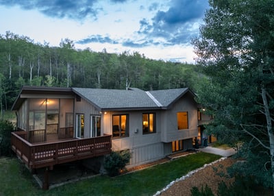 This spacious home features large windows and outdoor space, set against a lush, wooded backdrop.