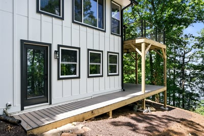 Modern home featuring a spacious deck with lake views, surrounded by lush greenery and nature.