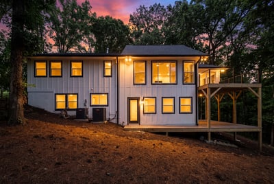 Modern two-story home surrounded by nature, featuring large windows and a spacious deck for outdoor living.