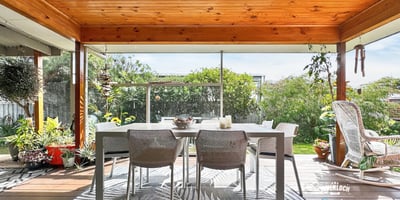 Spacious covered patio surrounded by lush greenery, perfect for outdoor dining and relaxation.