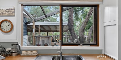 Bright kitchen featuring a large window that overlooks a spacious backyard with mature trees.