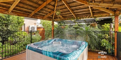 Relax in this private hot tub surrounded by lush landscaping under a rustic wooden pergola.