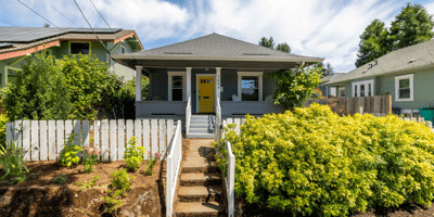 This inviting home features a vibrant yellow door, lush landscaping, and a welcoming front porch.