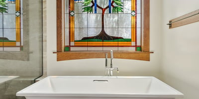 Relaxing soaking tub framed by decorative stained glass and warm wood trim. This peaceful bathroom retreat blends artistry with luxury finishes.