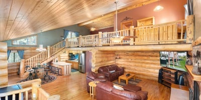 Bright great room with vaulted ceilings, hardwood floors, and exposed log beams. The open layout offers flexible living and entertaining space.