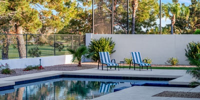 Relax in the backyard retreat featuring a sparkling pool, lounge seating, and serene views framed by mature landscaping.