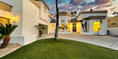 The home s crisp white exterior glows against a vibrant Scottsdale sunset, surrounded by palms and a pristine front lawn.