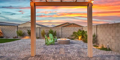 The fire pit area shines under sunset skies, surrounded by Adirondack chairs, desert plants, and durable pavers. A great space for evening gatherings in Litchfield Park.