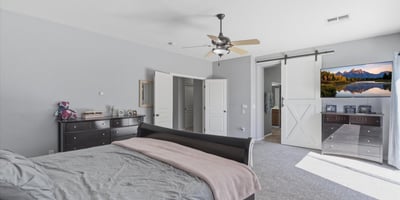 Elegant primary bedroom with barn-style sliding door access to the bathroom, spacious layout, and soft carpeting for a comfortable and stylish retreat.