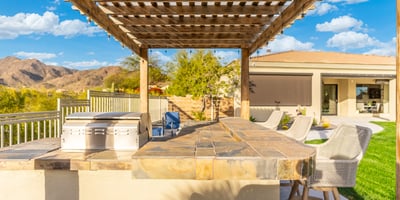 Scottsdale backyard kitchen with stone counters, grill, and seating under pergola, ideal for gatherings and outdoor dining.