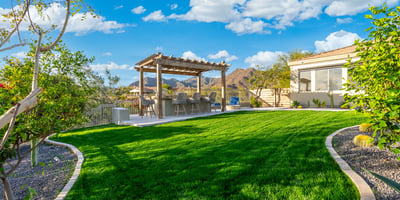 Scottsdale backyard with green lawn, pergola-covered kitchen, and scenic mountain backdrop, perfect for entertaining.