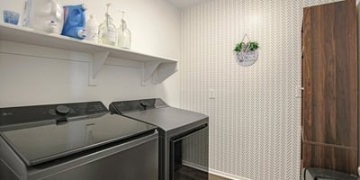 Well-appointed laundry room featuring stylish wallpaper, modern flooring, upper shelving, and dedicated space for laundry appliances. A practical upgrade for everyday living in this Waddell home.