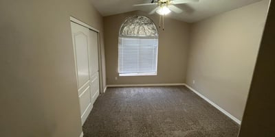 Featuring soft carpeting, a ceiling fan, an arched window, and ample closet space, this inviting bedroom offers flexibility for guests, family, or a home office.
