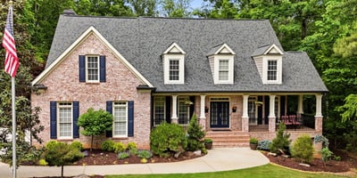 Beautiful brick home nestled in nature, featuring a spacious porch and well-maintained landscaping in a peaceful setting.