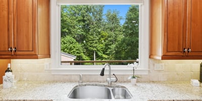 Bright kitchen featuring rich wood cabinetry and a scenic view of lush greenery through a large window.