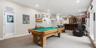 Spacious recreational room featuring a pool table and a well-equipped bar, perfect for entertaining.