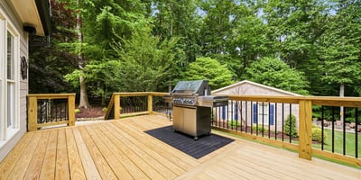 Spacious deck featuring a built-in grill, perfect for outdoor entertaining amid a lush, wooded backdrop.