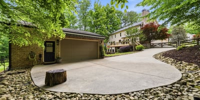 Spacious driveway with natural landscaping offers a welcoming approach to this unique property surrounded by trees.