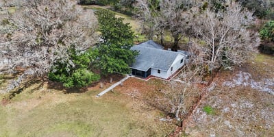 Aerial photo of the house with a front sidewalk as well as a rear entry sidewalk located off of the two car garage and paved slab parking area. This home is surrounded by mature trees and landscaping!