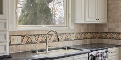 Modern kitchen featuring sleek countertops, ample cabinetry, and a window overlooking a lush outdoor space.