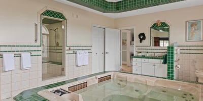 Spacious bathroom featuring a luxurious jetted tub, large walk-in shower, and distinctive green tile accents.