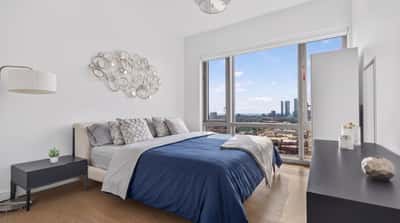 Bright bedroom featuring large windows with stunning city views and modern furnishings for comfortable living.