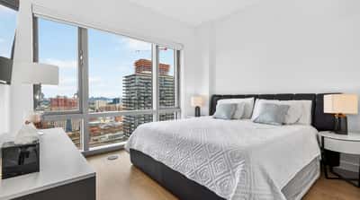 Bright bedroom featuring modern design, floor-to-ceiling windows, and stunning city skyline views. Perfect for urban living.