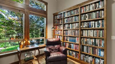 Bright reading nook featuring a cozy chair, built-in bookshelf, and large windows with garden views.