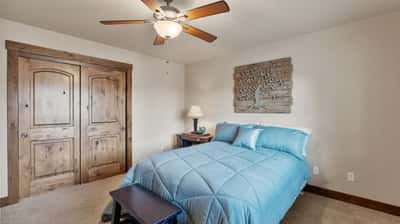 Cozy bedroom featuring a ceiling fan, natural wood accents, and ample storage with double doors.