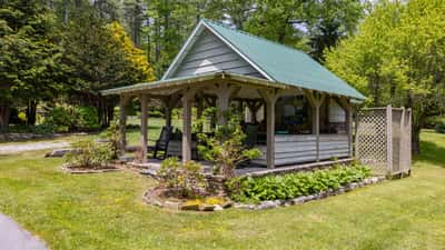 Cozy cottage with a green metal roof, surrounded by lush gardens and inviting outdoor seating.