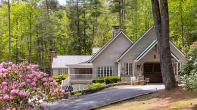 Nestled among lush greenery, this inviting home features a spacious driveway and warm outdoor gathering areas.