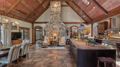Spacious open-concept kitchen and dining area featuring a striking stone fireplace and rustic wooden beams.