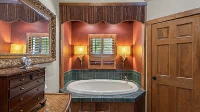Relax in this inviting bathroom featuring a corner tub, warm lighting, and rich wooden accents.