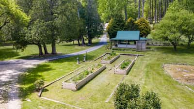Spacious outdoor space featuring raised garden beds, a cozy gazebo, and lush greenery, ideal for gardening enthusiasts.
