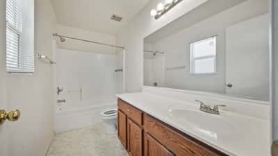 Ensuite bathroom features a long vanity, oversized mirror, combination tub and shower, and natural light. Designed with comfort, convenience, and everyday functionality in mind.